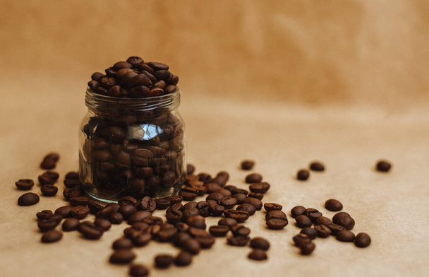 Coffee beans in a glass jar. Dark-colored roasted coffee beans on Kraft paper. Texture. - Zdjęcie, obraz