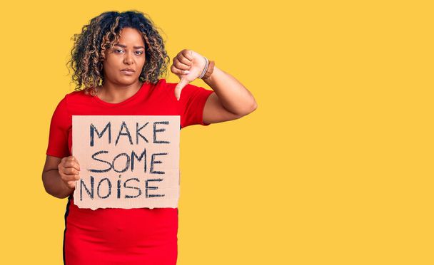 Young african american plus size woman holding make some noise banner with angry face, negative sign showing dislike with thumbs down, rejection concept  - Photo, Image
