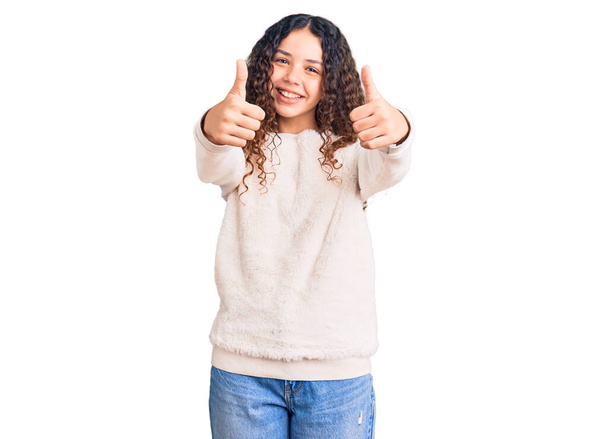 Schöne junge Mädchen mit lockigen Haaren tragen lässige Kleidung zustimmend positive Geste mit der Hand, Daumen nach oben lächelnd und glücklich über den Erfolg. Siegergeste.  - Foto, Bild