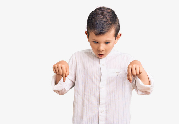 Criança loira bonito vestindo camisa elegante apontando para baixo com os dedos mostrando propaganda, rosto surpreso e boca aberta  - Foto, Imagem