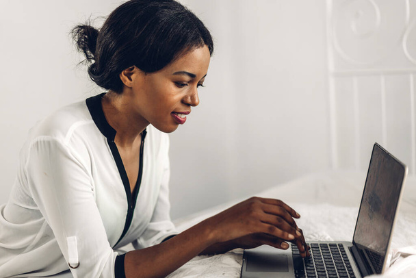 Портрет усміхненої щасливої афроамериканської чорної жінки, яка розслабляється за допомогою технології ноутбука, сидячи на столі. Молода творча африканська дівчина працює вдома. робота з домашньої концепції
 - Фото, зображення