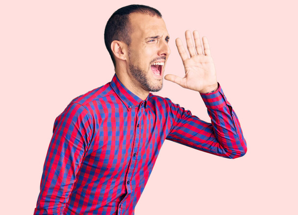 Jonge knappe man draagt nonchalante kleren schreeuwend en schreeuwend naast elkaar met hand op mond. communicatieconcept.  - Foto, afbeelding