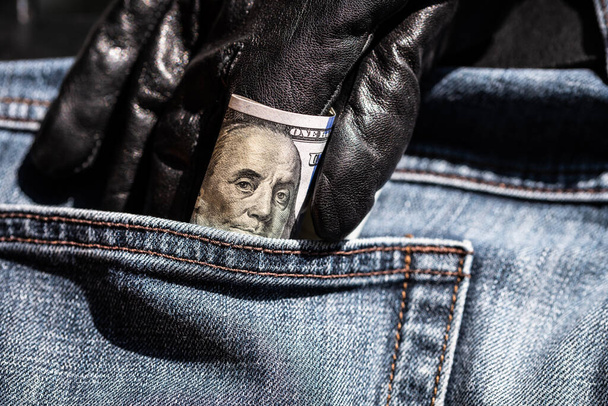 Fragment of a hundred dollar banknote. Hand in black glove pulls out a dollar bill from his pocket jeans - Foto, Bild