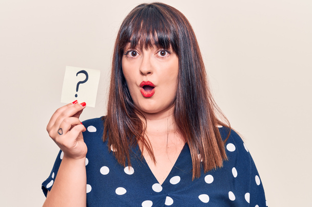 Young plus size woman holding question mark scared and amazed with open mouth for surprise, disbelief face  - Photo, Image
