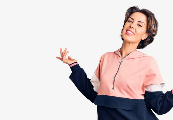 Jovem mulher bonita vestindo sportswear sorrindo mostrando ambas as mãos palmas abertas, apresentando e publicidade comparação e equilíbrio  - Foto, Imagem