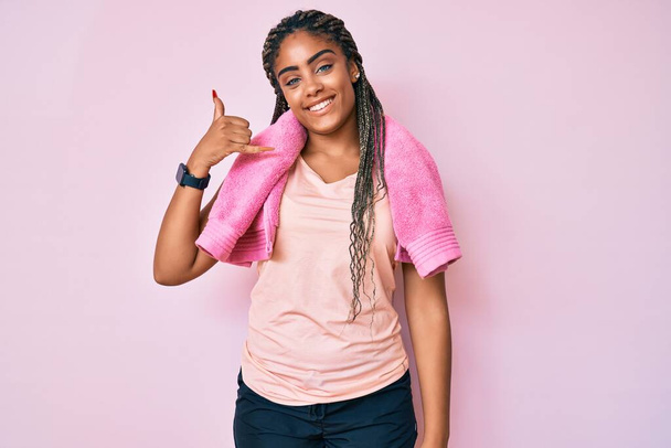 Jonge Afro-Amerikaanse vrouw met vlechten in sportkleding en handdoek lachend telefoongebaar met hand en vingers zoals telefoneren. communicatie van concepten.  - Foto, afbeelding