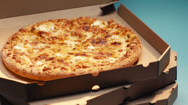 Deliciosa pizza con queso en cajas de cartón sobre fondo azul - Metraje, vídeo