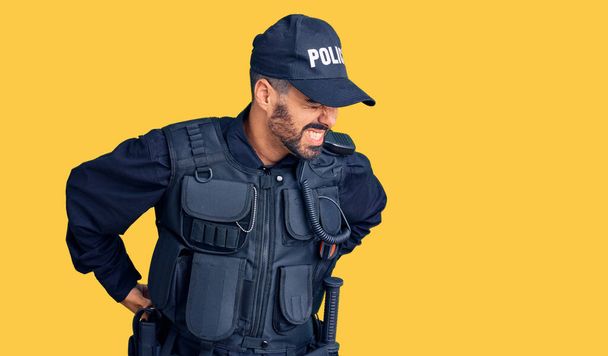 Junger hispanischer Mann in Polizeiuniform leidet unter Rückenschmerzen, Berührung mit der Hand, Muskelschmerzen  - Foto, Bild