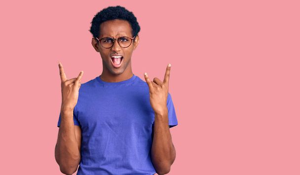 Afričan pohledný muž v neformálním oblečení a brýlích křičí s bláznivým výrazem a dělá rockový symbol s rukama nad hlavou. hudební hvězda. těžký koncept.  - Fotografie, Obrázek