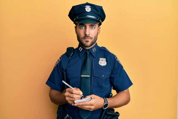 Handsome hispanic man wearing police uniform writing traffic fine relaxed with serious expression on face. simple and natural looking at the camera.  - Фото, изображение