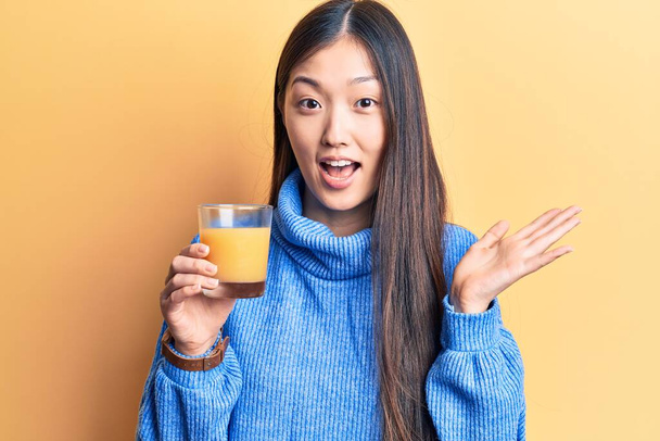 Genç ve güzel Çinli kadın bir bardak portakal suyu içerek başarıyı mutlu bir gülümsemeyle ve kazanan yüz ifadesiyle kutluyor.  - Fotoğraf, Görsel