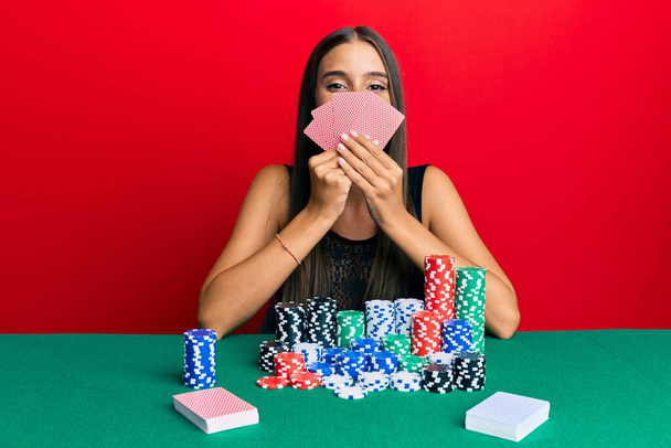 Yüzünde mutlu ve havalı bir gülümseme olan kart ile kumar maskesiyle poker oynayan genç İspanyol kadın. diş gösterme.  - Fotoğraf, Görsel