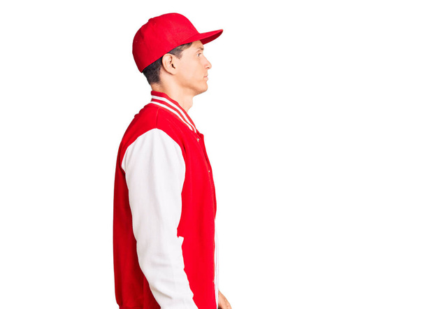 Junger gutaussehender Mann in Baseball-Uniform, der zur Seite schaut, entspannte Profil-Pose mit natürlichem Gesicht und selbstbewusstem Lächeln.  - Foto, Bild
