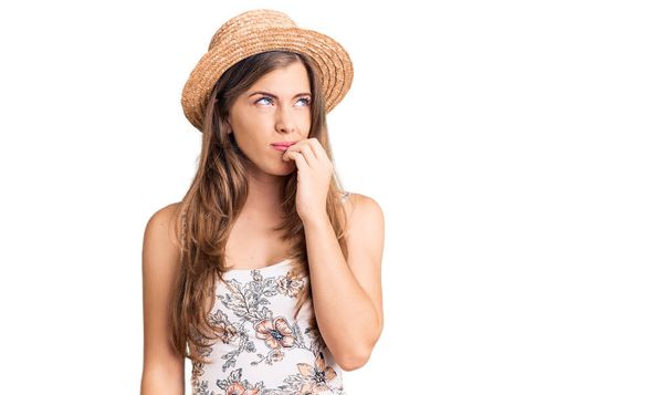 Krásná kavkazská mladá žena v letním klobouku vypadá vystresovaně a nervózně s rukama na ústech a kouše nehty. úzkostný problém.  - Fotografie, Obrázek