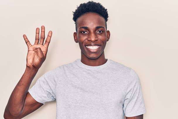 Молодий афроамериканець, одягнений у повсякденний одяг, показує і вказує вгору пальцями номер чотири, посміхаючись впевнено і щасливо.  - Фото, зображення