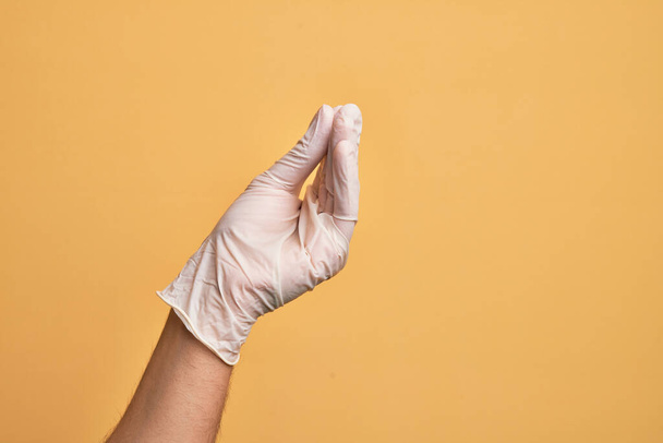 Hand of caucasian young man with medical glove over isolated yellow background doing Italian gesture with fingers together, communication gesture movement - Foto, afbeelding