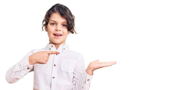 Schattig Latijns-Amerikaans kind draagt casual kleding verbaasd en glimlachend naar de camera terwijl presenteren met de hand en wijzen met de vinger.  - Foto, afbeelding