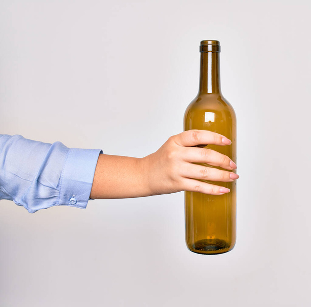Hand of caucasian young woman holding empty glass botlle of wine over isolated white background - Фото, изображение