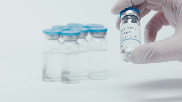 napisy szczepionek koronawirusowych na butelce w ręku naukowca na białym - Materiał filmowy, wideo