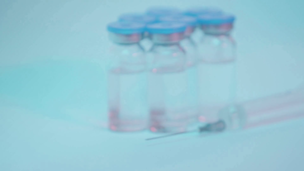коронавирусная вакцина на бутылке рядом с ученым в латексной перчатке на голубом - Кадры, видео
