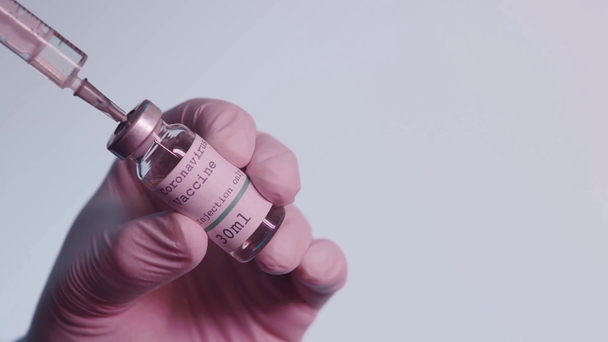 butelka ze szczepionką przeciw koronawirusowi w rękach osoby ze strzykawką wyizolowaną na szaro - Materiał filmowy, wideo
