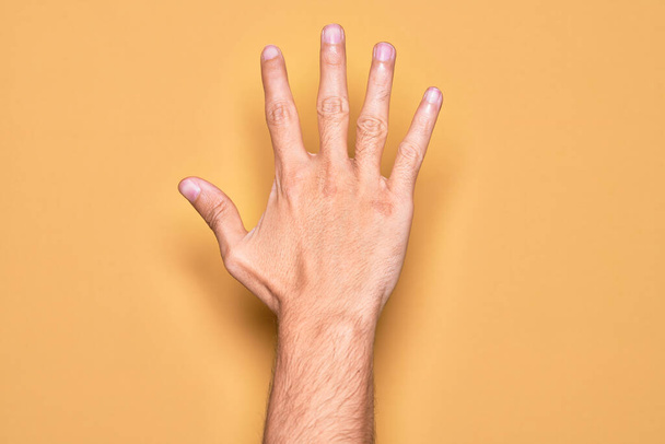 Рука кавказького молодого чоловіка, що показує пальці над ізольованим жовтим тлом, підраховуючи число 5 з п'ятьма пальцями
 - Фото, зображення