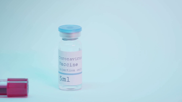 éprouvette avec échantillon de sang et flacon avec vaccin contre le coronavirus sur fond bleu - Séquence, vidéo