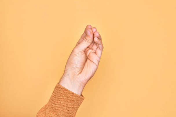 Hand des kaukasischen jungen Mannes zeigt Finger über isoliertem gelben Hintergrund und macht italienische Geste mit den Fingern zusammen, Kommunikationsgeste Bewegung - Foto, Bild