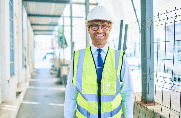 Business architect man wearing hardhat standing outdoors of a building project wearing reflective vest - Zdjęcie, obraz