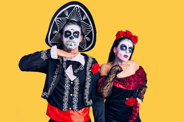 Young couple wearing mexican day of the dead costume over background cutting throat with hand as knife, threaten aggression with furious violence  - Фото, зображення