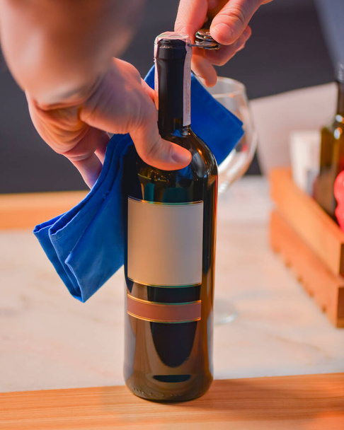 Wine glass and bottle of red wine on a wooden table over blurred background. Restaurant service, eating out concept. Drinking alcohol in a restaurant, celebration. Man, waiter opens a bottle of wine. - Foto, Bild