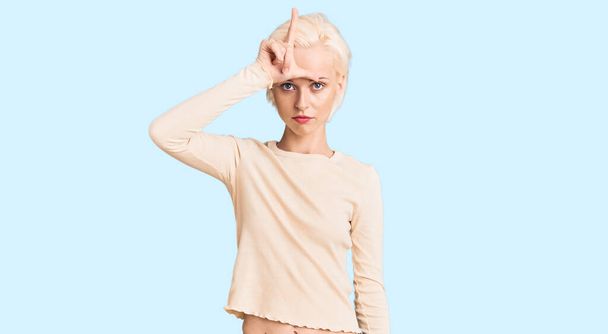 Young blonde woman wearing casual clothes making fun of people with fingers on forehead doing loser gesture mocking and insulting.  - Photo, Image