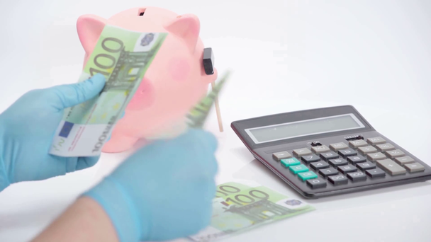 Muž počítání eurobankovky v blízkosti prasátko banky a kalkulačka na bílém pozadí - Záběry, video