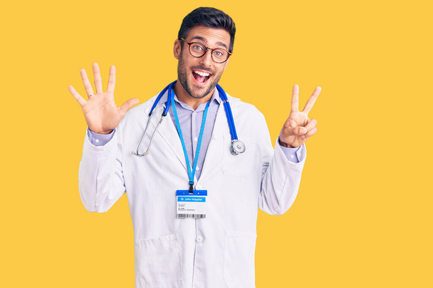 Junger hispanischer Mann trägt Doktoruniform und Stethoskop und zeigt mit Finger Nummer sieben nach oben, während er selbstbewusst und glücklich lächelt.  - Foto, Bild
