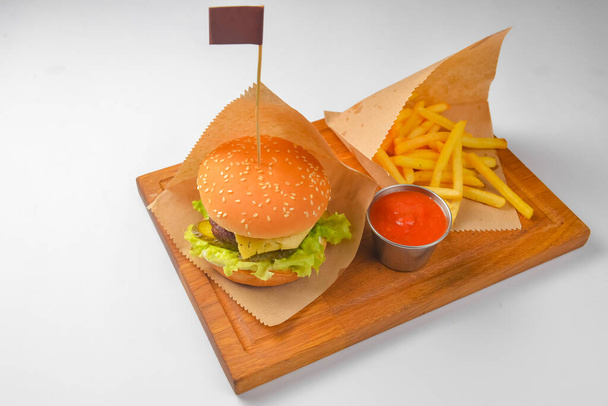 Hamburger with french fries and tomato dip sauce. Fast food, junk food concept. Served on a rustic wooden board over white background. Close up. - Foto, immagini