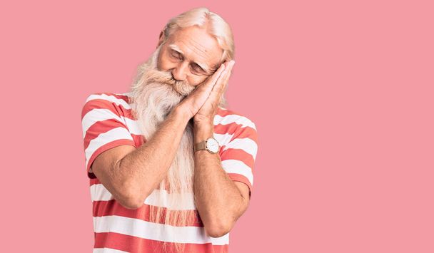 Homem idoso com cabelos grisalhos e barba comprida vestindo tshirt listrada dormindo cansado sonhando e posando com as mãos juntas enquanto sorri com os olhos fechados.  - Foto, Imagem