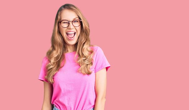 Young beautiful caucasian woman with blond hair wearing casual clothes and glasses winking looking at the camera with sexy expression, cheerful and happy face.  - Photo, Image
