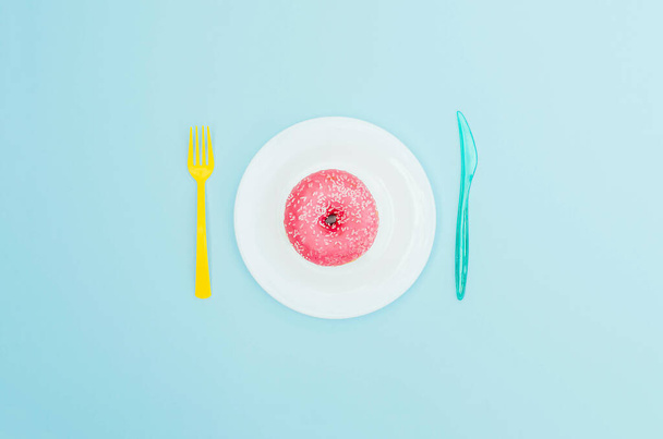 Vaaleanpunainen donitsi sinisellä lautasella ja vaaleansininen tausta. Makeaa ja herkullista ruokaa. - Valokuva, kuva