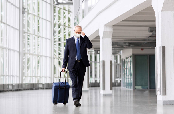 old businessman in mask with travel bag at airport - Foto, imagen