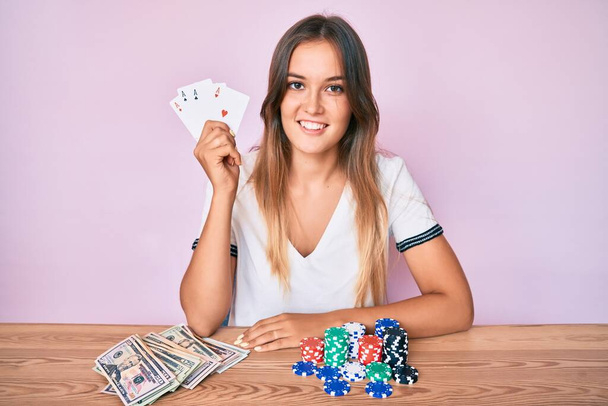 Belle femme caucasienne jouant au poker tenant des cartes regardant positif et heureux debout et souriant avec un sourire confiant montrant des dents  - Photo, image