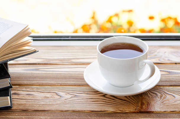 Una taza de té se encuentra en un alféizar de madera contra la ventana - Foto, imagen