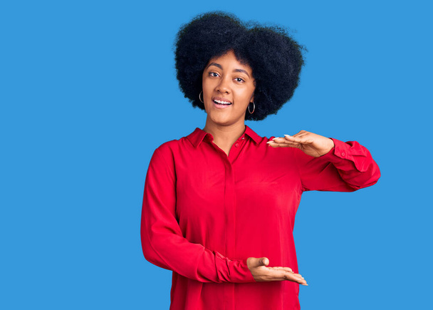 A fiatal afro-amerikai lány alkalmi ruhát visel gesztikuláló kezek mutatják nagy és nagy méretű jel, intézkedés szimbólum. mosolyogva néz a kamerába. mérési koncepció.  - Fotó, kép