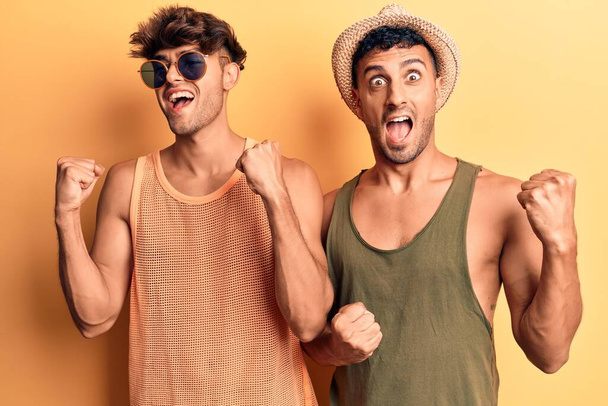 Mladý homosexuální pár v letních šatech slaví překvapení a úžas nad úspěchem se zdviženýma rukama a otevřenýma očima. koncept vítěze.  - Fotografie, Obrázek