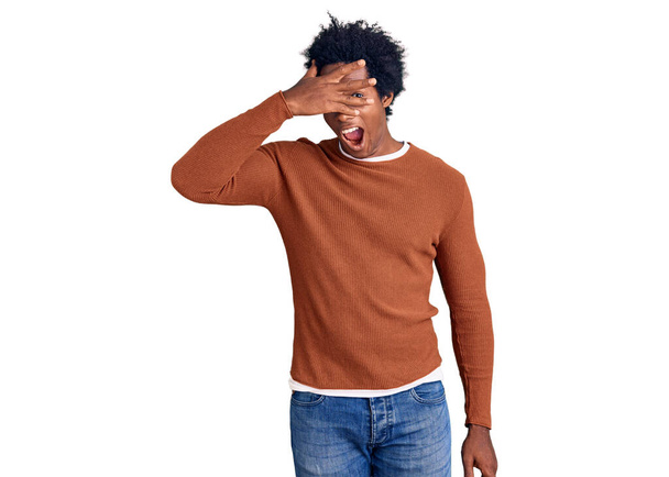 Knappe Afro-Amerikaanse man met afro haar in casual kleren gluren in shock bedekken gezicht en ogen met de hand, kijken door vingers met beschaamde uitdrukking.  - Foto, afbeelding