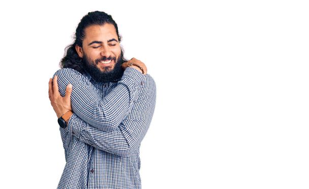 Junger arabischer Mann in lässiger Kleidung, der sich glücklich und positiv umarmt und selbstbewusst lächelt. Selbstliebe und Selbstfürsorge  - Foto, Bild