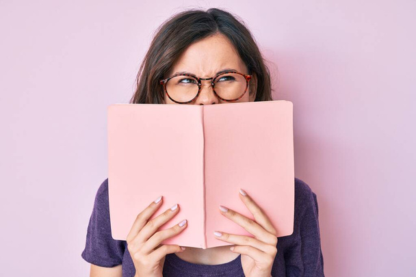 Young beautiful woman wearing glasses reading book angry and mad screaming frustrated and furious, shouting with anger. rage and aggressive concept.  - Photo, Image