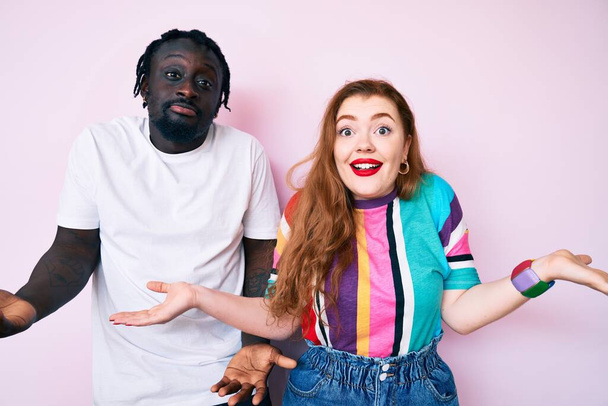 Couple Interracial portant des vêtements décontractés souriant montrant les paumes ouvertes des deux mains, présentant et comparant la publicité et l'équilibre  - Photo, image