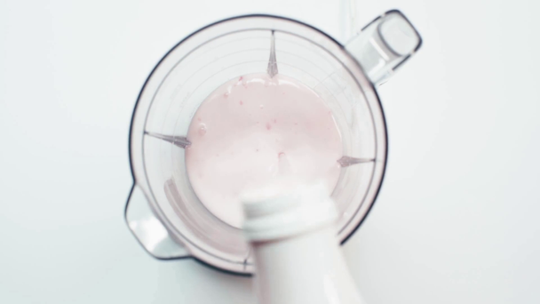 Horní pohled na jogurt nalévání v mixéru na bílém - Záběry, video