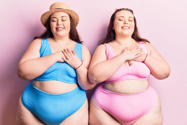Young plus size twins wearing bikini smiling with hands on chest with closed eyes and grateful gesture on face. health concept.  - Photo, Image