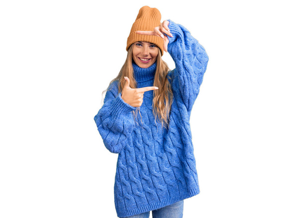 Красивая кавказская женщина с светлыми волосами в шерстяном свитере и зимней шляпе улыбается, делая рамку с руками и пальцами с счастливым лицом. креативность и концепция фотографии.  - Фото, изображение